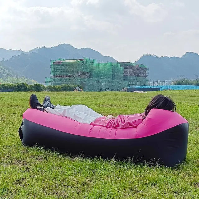 Pink and black Relax™ Inflatable Sofa Bed with a person reclining in a scenic outdoor setting. Comfortable and easy to inflate for travel convenience.