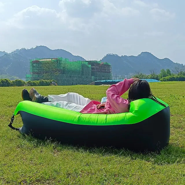 Green and black Relax™ Inflatable Sofa Bed with a person reclining in a scenic outdoor setting. Comfortable and easy to inflate for travel convenience.