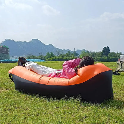 Orange and black Relax™ Inflatable Sofa Bed with a person reclining outdoors. Comfortable and portable, great for camping and picnics.