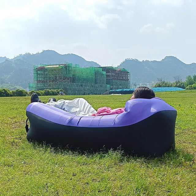 Purple and black Relax™ Inflatable Sofa Bed with a person lounging in a grassy field. Ideal for outdoor relaxation and travel.